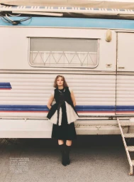 Model Fran Summers wearing a black sleeveless top with a flared white trim standing against a white vintage trailer.
