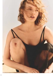Model Fran Summers squatting in a black slip dress with windblown wavy hair and a scraped knee in warm natural light.