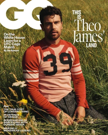 Theo James wearing a red and peach vintage-style jersey with the number 39 sits in a tall grassy field for a magazine cover portrait.