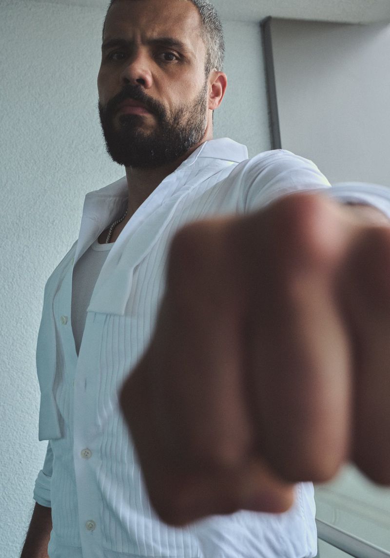 Close-up of Howard Charles wearing a white button-down shirt, looking directly at the camera with his right fist extended forward.
