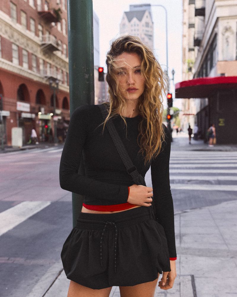Model posing in a black long-sleeve top and matching black mini puff skirt on an urban city street with crosswalk.