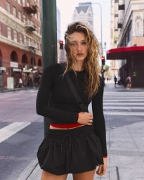 Model posing in a black long-sleeve top and matching black mini puff skirt on an urban city street with crosswalk.