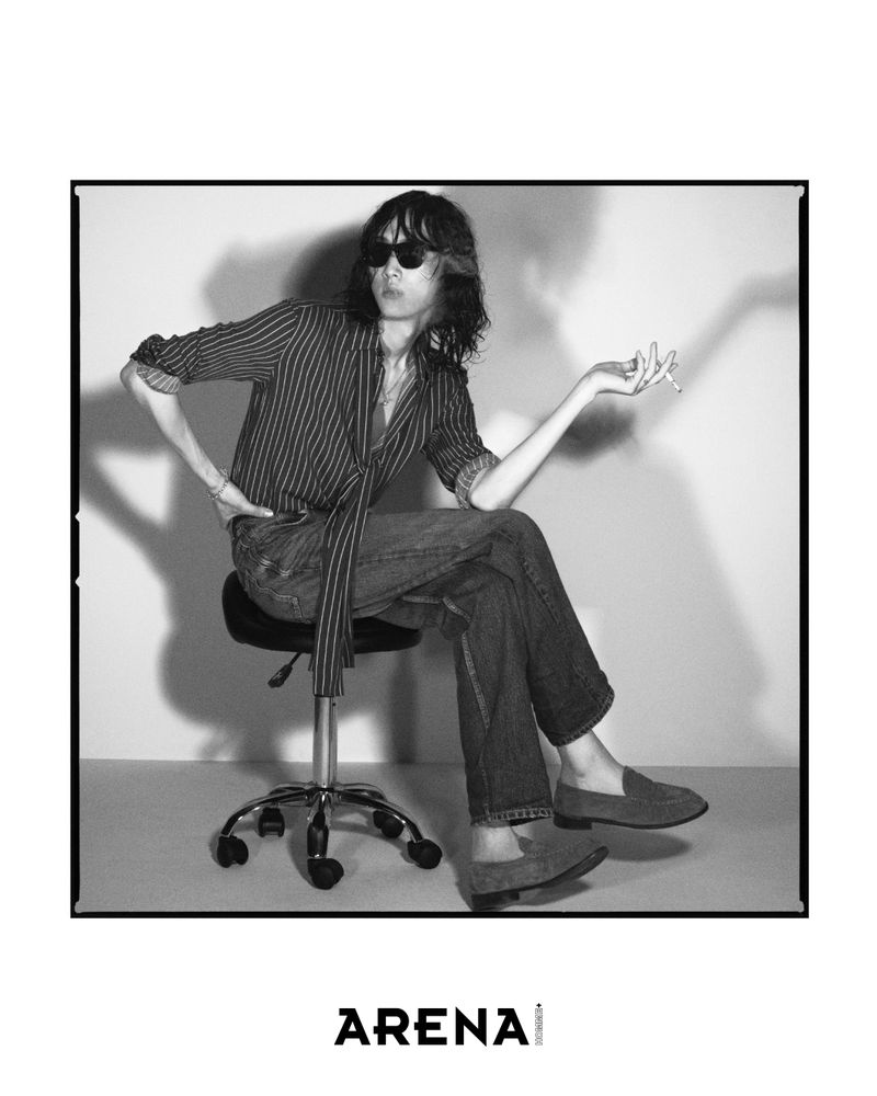 Model Han Ji seated on a swivel stool wearing sunglasses, a striped shirt, and denim jeans against a plain studio wall.