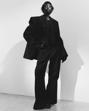 Model Aluk Malual wearing an oversized black suit against a white wall in a fashion editorial for 10 Magazine Deutsch.