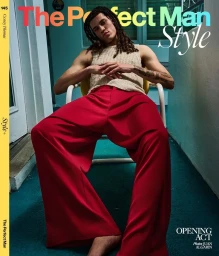 Model Corey Thomas seated in wide-leg red trousers and a cream knit vest on a teal balcony for a magazine cover.