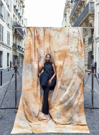 Fashion shot in urban setting of woman in patterned top and black skirt standing in front of tie-dye textile and metal frame.