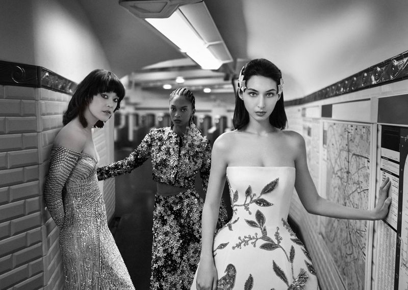 Three fashion models pose in evening gowns in a subway station. Black and white image with artistic photography and elegant couture.