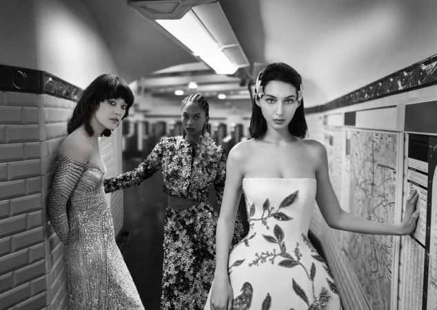 Three fashion models pose in evening gowns in a subway station. Black and white image with artistic photography and elegant couture.