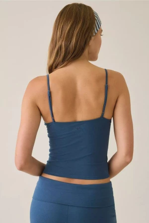 Rear view of a woman wearing a petrol blue camisole and matching bottoms with a striped headband against a neutral backdrop.