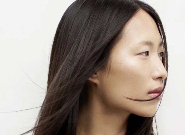 Close-up portrait of a serene Asian woman with long, dark hair against a bright white background, focusing on beauty and hair texture.