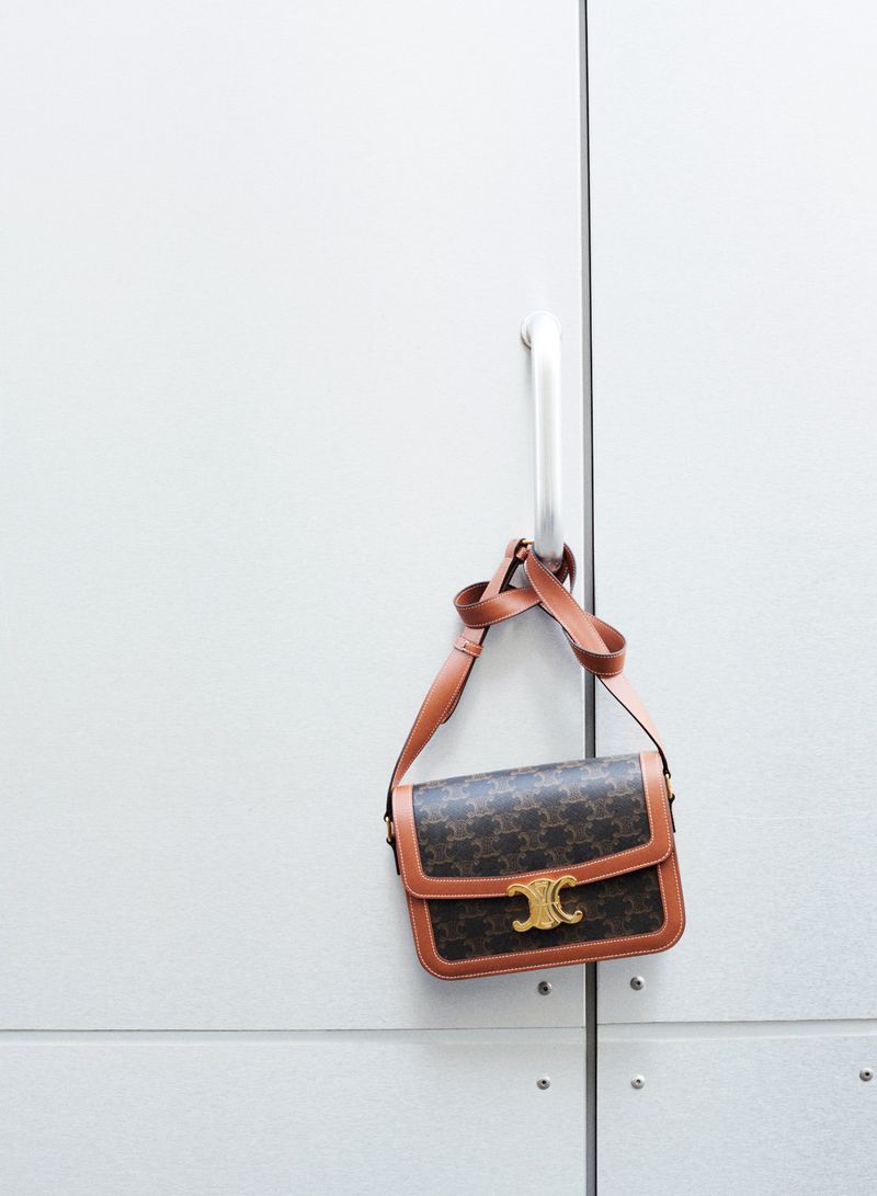 Celine handbag hangs from a metal door handle against a white door, a luxury fashion accessory in a studio setting.