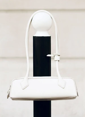 A white handbag hanging on a black and white bollard against a neutral background.