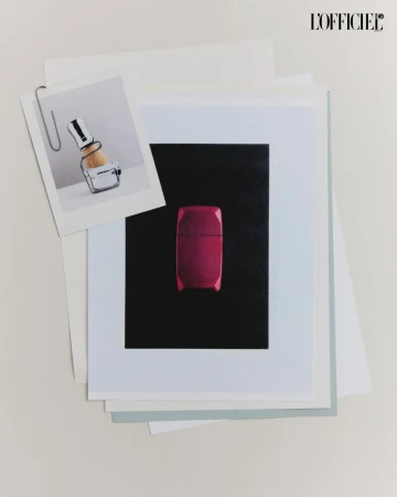 Still life of photographs and paper, featuring a pink cosmetic case and a shaving brush attached with a silver paper clip.