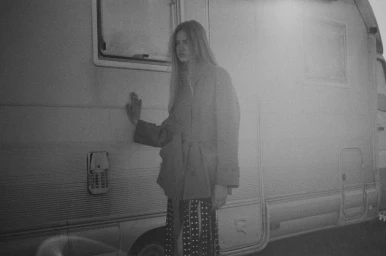 Black and white photograph of a woman with long hair resting her hand on the side of a camper van.