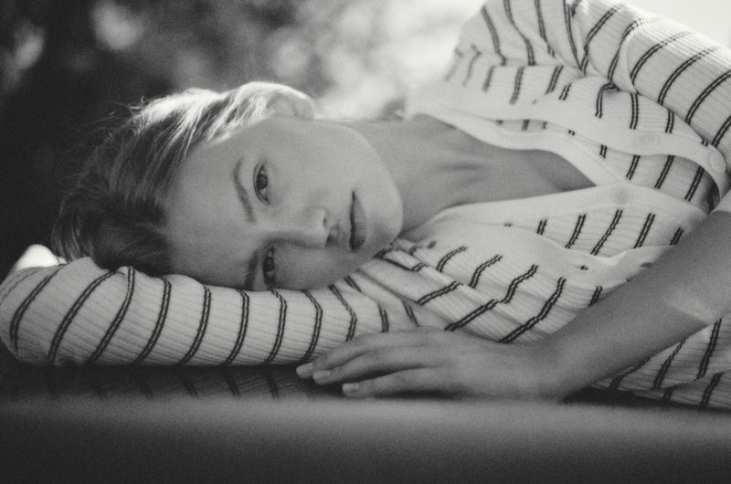 Black and white portrait of a woman lying down wearing a striped ribbed knit cardigan and looking directly at the camera.