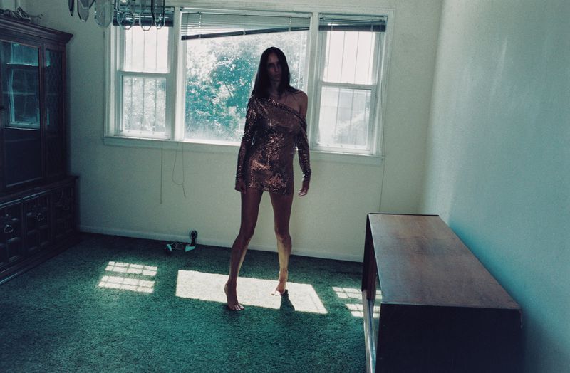 Model Waleska Gorczevski standing barefoot in a sequined mini dress inside a room with green carpet and large windows.