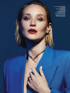 Close-up portrait of a woman in a vibrant royal blue blazer with slicked-back blonde hair, red lipstick, and a metallic choker necklace.