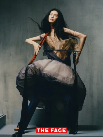 Model Sui He posing in a layered sculptural tulle gown against a textured grey studio wall.