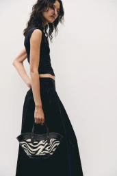 Model wearing a black top and skirt holding a zebra print handbag against a white background