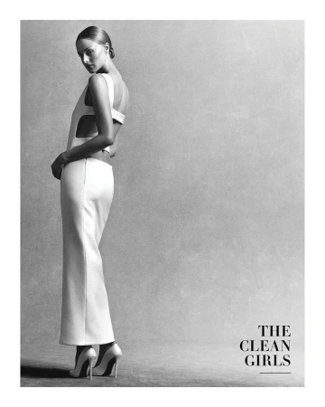 Full-length black and white portrait of a woman in a backless white dress and stilettos looking over her shoulder against a grey backdrop.