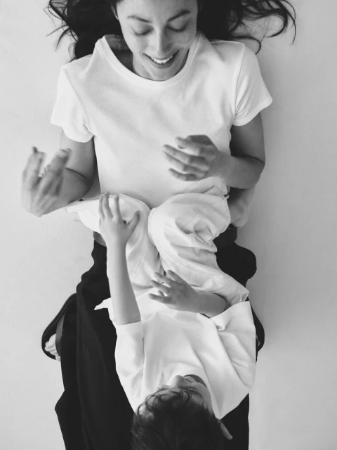 A mother and child are lying on their backs indoors, the mother smiling, in this overhead monochrome shot showcasing family time.