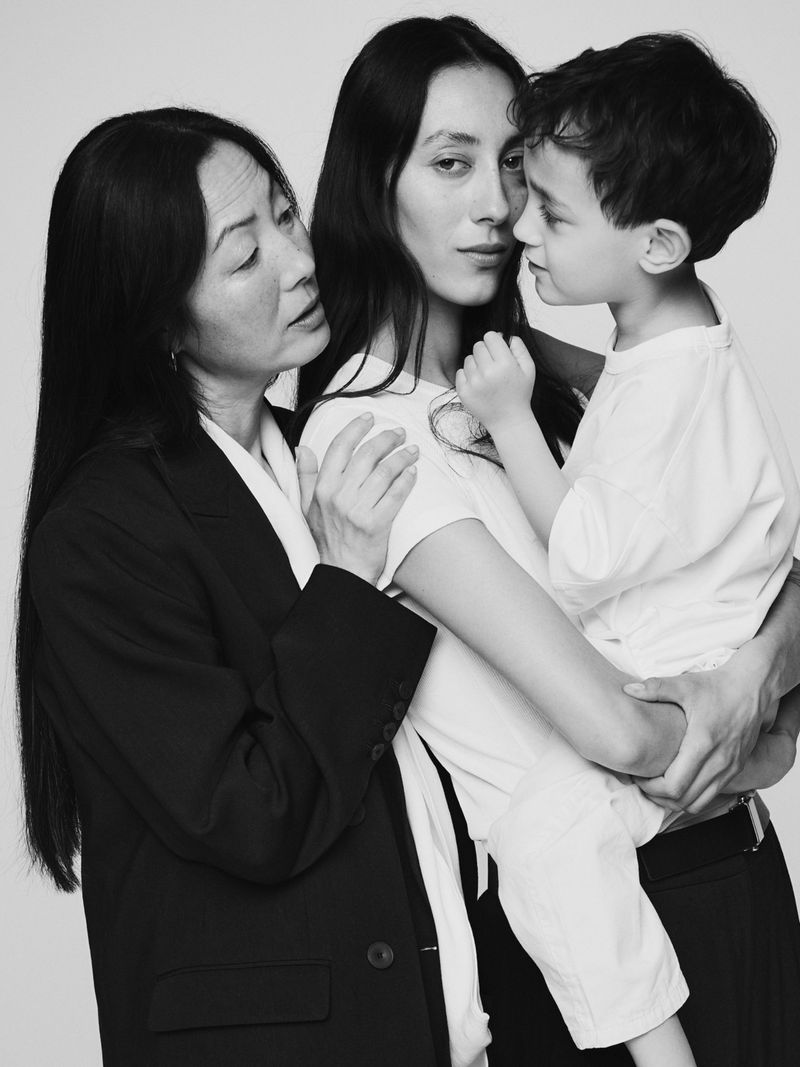 Monochrome portrait of an Asian woman, a young woman, and a child in a studio, showcasing intergenerational connections and minimalist fashion.