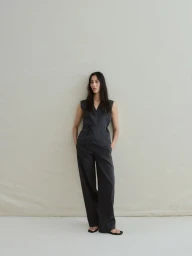 Model standing against a plain light background wearing a dark sleeveless vest top and matching trousers.