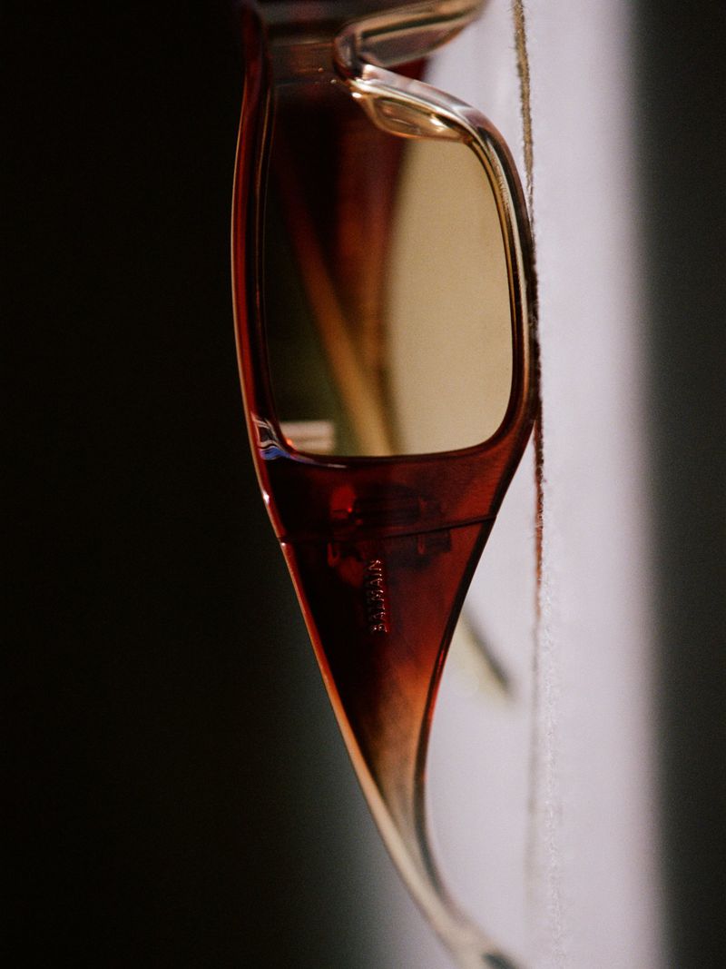 Close-up of amber tortoiseshell sunglasses with a yellow tinted lens and engraved temple arm against a split studio backdrop.