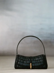 Dark crocodile-embossed luxury handbag with an arched top handle and gold clasp resting on a muted studio floor.