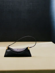 Black leather Balmain shoulder bag with gold-tone hardware resting on a neutral surface against a dark background.