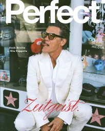 Josh Brolin crouching in an off-white suit and sunglasses with a toy parrot on his shoulder for Perfect Magazine cover.