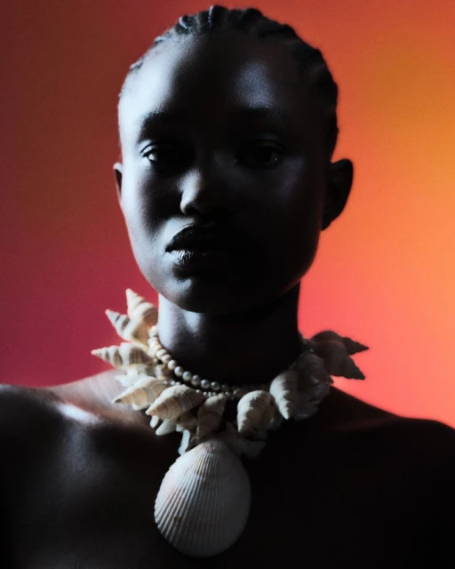 Elegant portrait of an African American woman wearing a shell necklace against a gradient orange and red background. Beauty shot. 