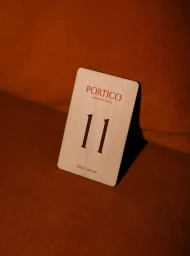Wooden hotel room key card numbered eleven for Portico Boutique Hotel resting on a rust-orange fabric surface.