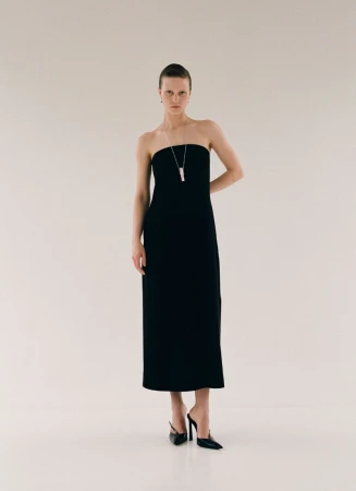 Model Sofia Hansson posing in a strapless black column dress, pendant necklace, and black pointed heels against a white backdrop.