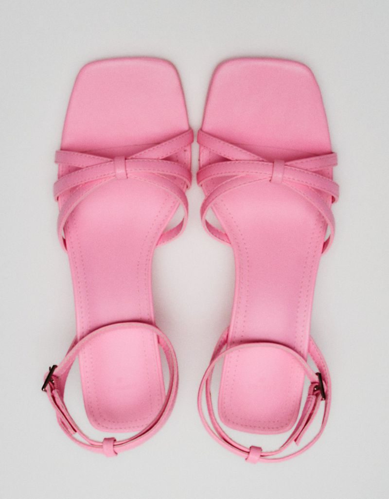 Overhead studio shot of a pair of open-toe, strappy, high-heel sandals in pink, with a buckle closure, on a solid white background.