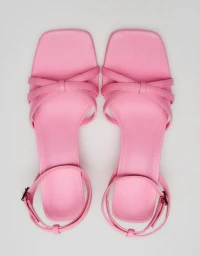 Top-down view of a pair of pink leather strappy sandals with square toes resting on a white background