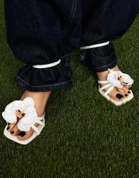 Close-up of feet wearing white heeled sandals with large white orchid flowers, standing on green grass