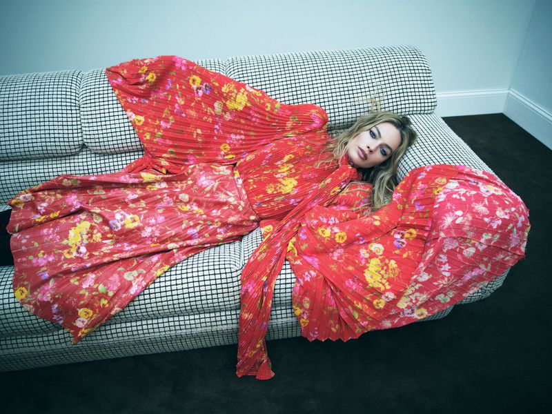 Blonde woman in floral dress lying on a checkered couch in a studio setting, creating a fashionable and relaxed editorial scene.