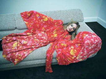 Margot Robbie lying on a houndstooth patterned sofa wearing a red floral pleated dress for Vogue Australia