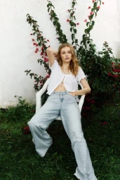 Model seated outdoors in a white top and light blue jeans against a white wall with blooming bougainvillea for H&M Malaga Lookbook