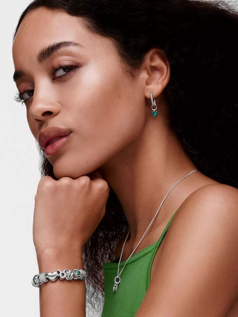 Close-up of a woman with dark hair wearing silver jewelry, including a bracelet with charms and a necklace with a pendant.
