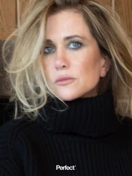 Close-up portrait of Kristen Wiig in a black ribbed turtleneck sweater with tousled blonde hair looking at the camera.