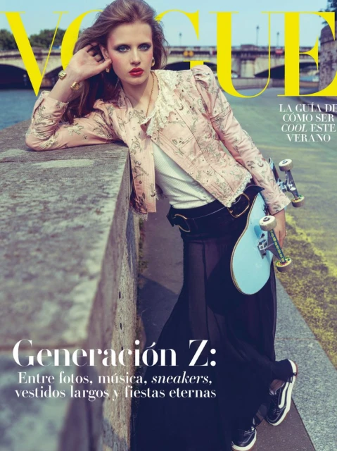 Vogue cover featuring a young adult female model in stylish clothing and accessories, posing with a skateboard on a city street near a river.