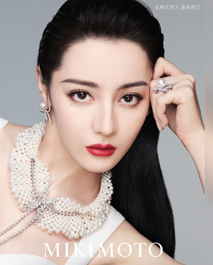 Dilraba Dilmurat wearing an ornate Mikimoto pearl collar necklace and pearl jewelry against a grey studio background.