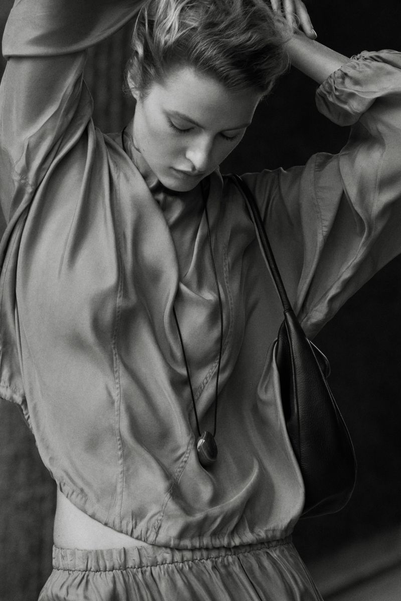 Model Felice Nova Noordhoff posing in a draped satin top, cord pendant necklace, and leather shoulder bag in black and white.