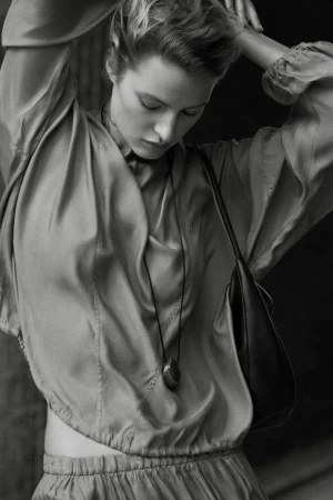 Model Felice Nova Noordhoff posing in a draped satin top, cord pendant necklace, and leather shoulder bag in black and white.