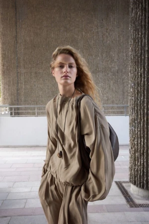 Felice Nova Noordhoff wearing a fluid taupe silk two-piece outfit with a shoulder bag against textured architectural walls.