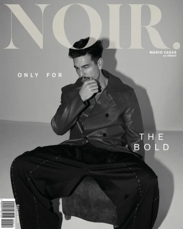 Black-and-white magazine cover shot of a man in a leather jacket and black pants, seated against a plain background, with overlaid text.