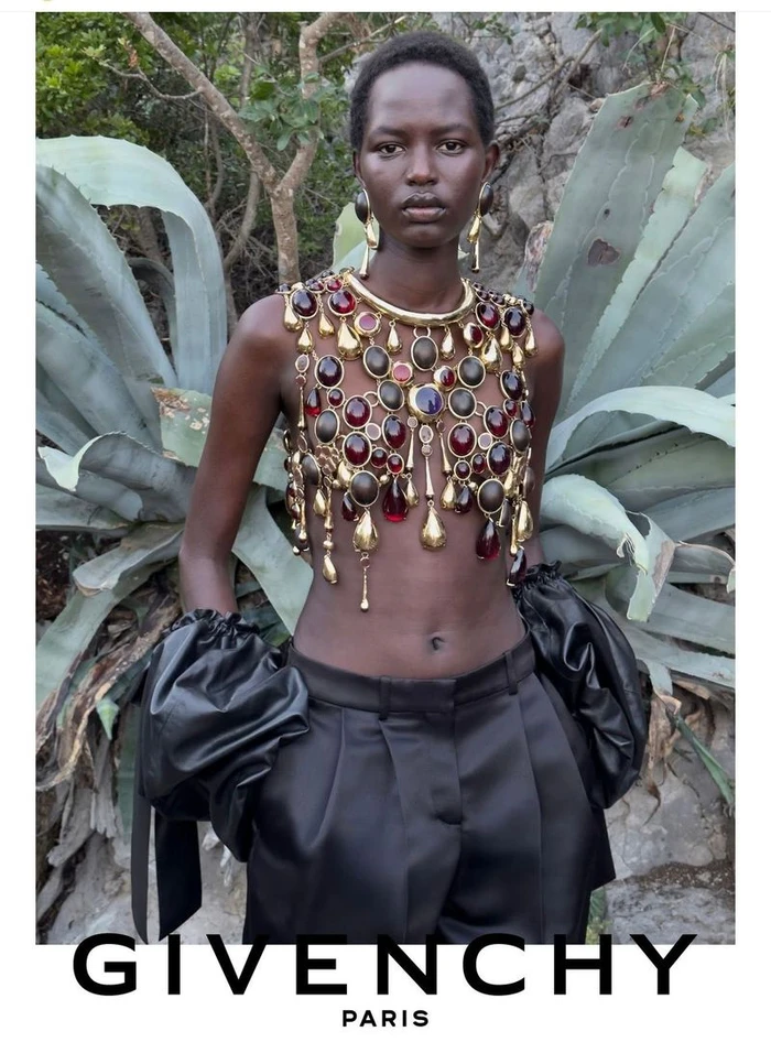 Model Nyaduola Gabriel wearing an ornate gold and gem-encrusted harness top with black satin trousers for Givenchy.
