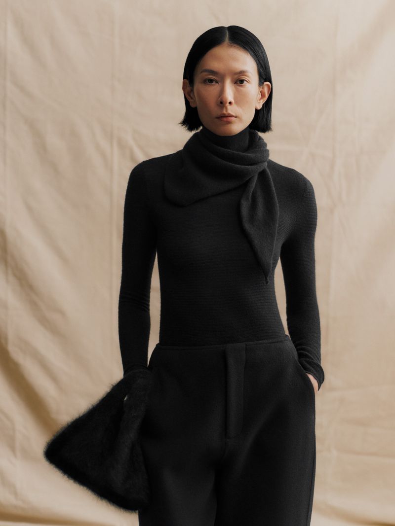 Model Hsin-Yu Liu wearing an all-black knit turtleneck top, matching wrap scarf, and trousers against a neutral textured backdrop.